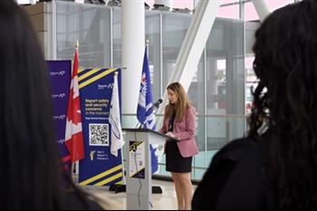 a woman speaking to a group of people in a room with flags