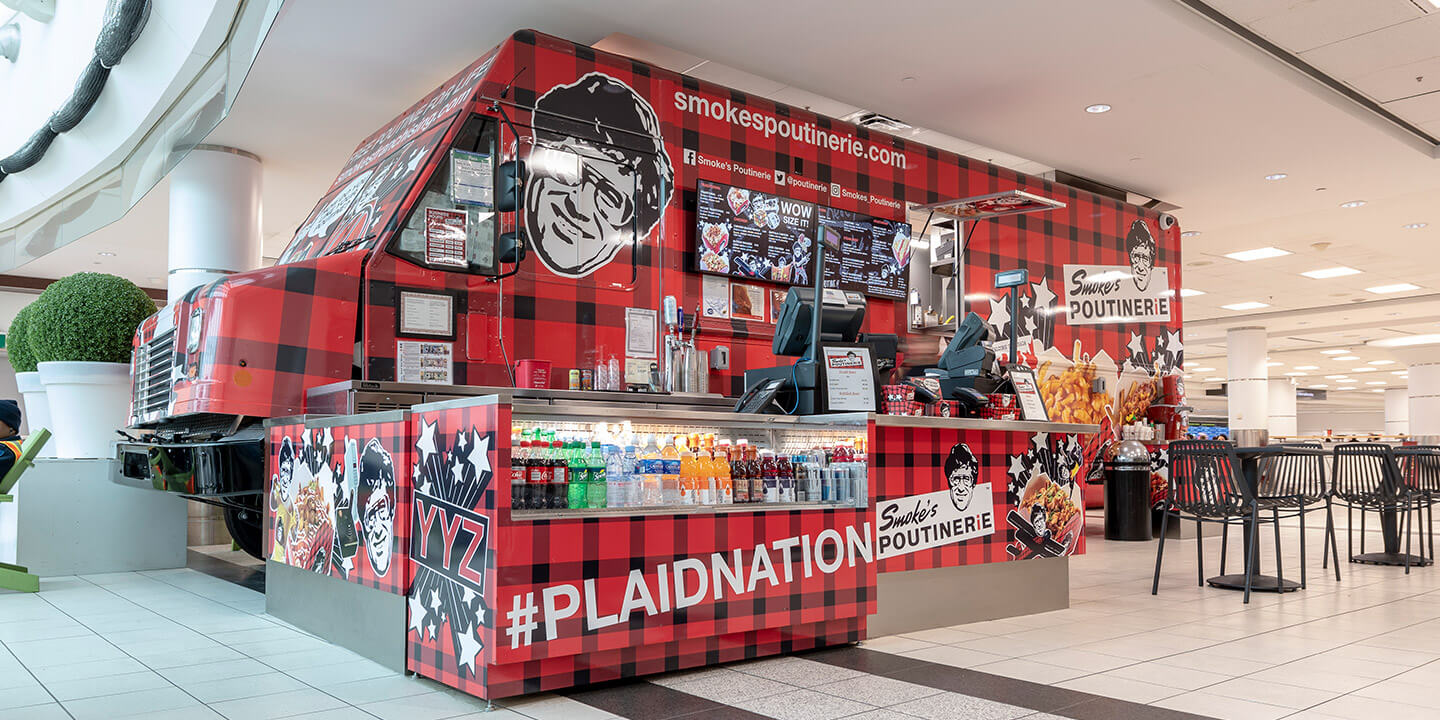 Smoke's Poutinerie counter with bold red plaid food truck backdrop 