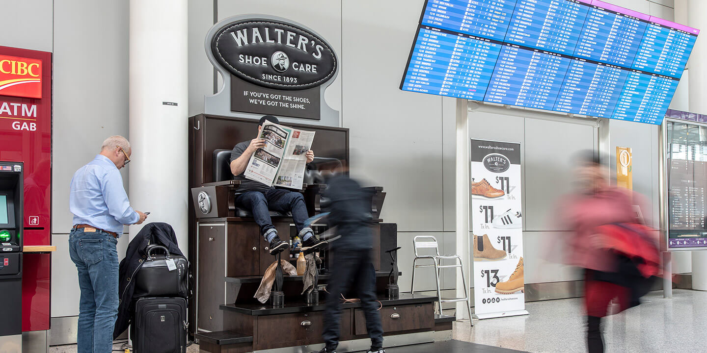 Man reading a newspaper while having his shoes shined at a Walter's Shoe Care kiosk.