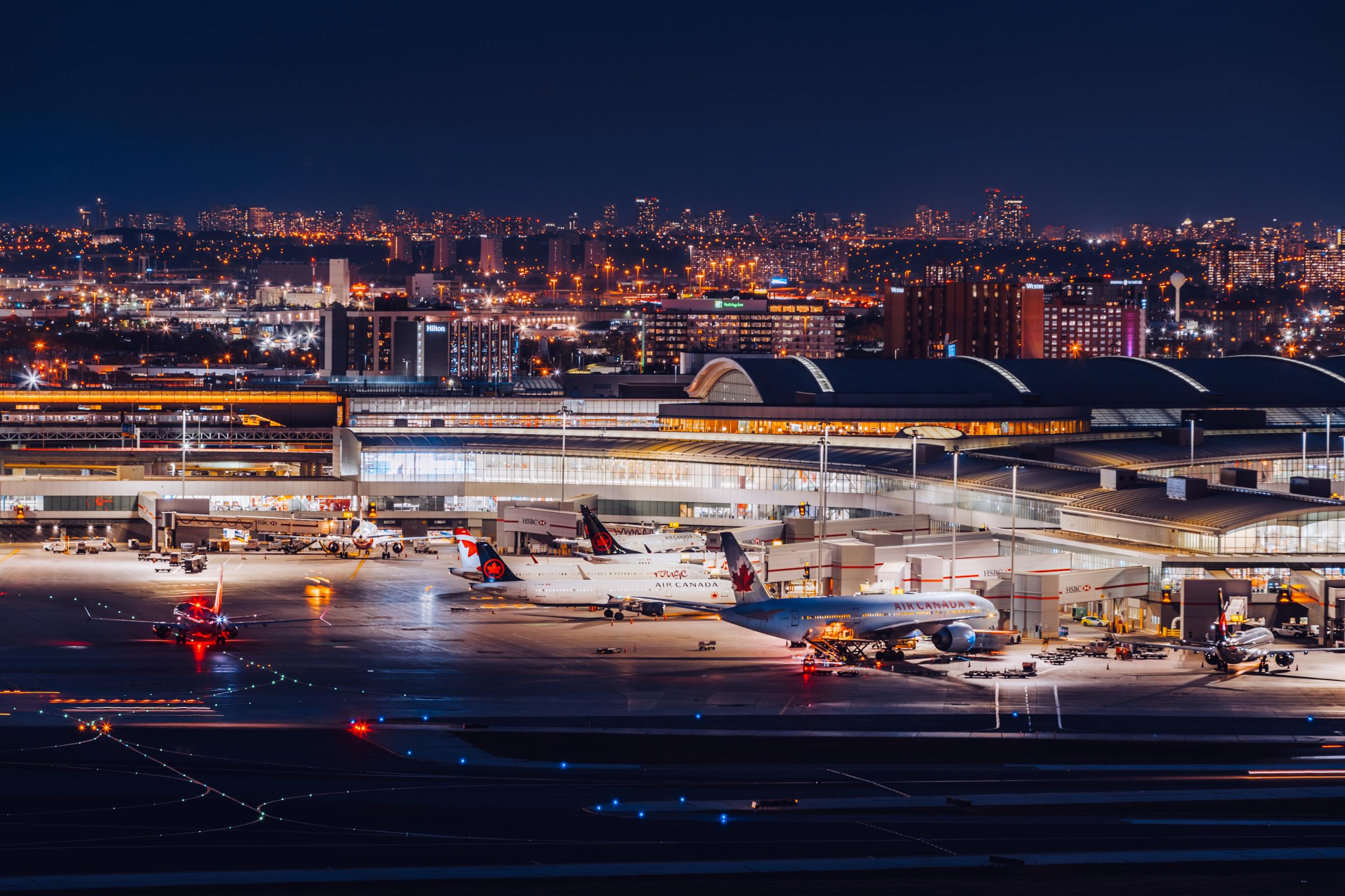 A night view of the Toronto Pearson airport. There are plans at the terminal in the foreground and downtown Toronto in the distance.