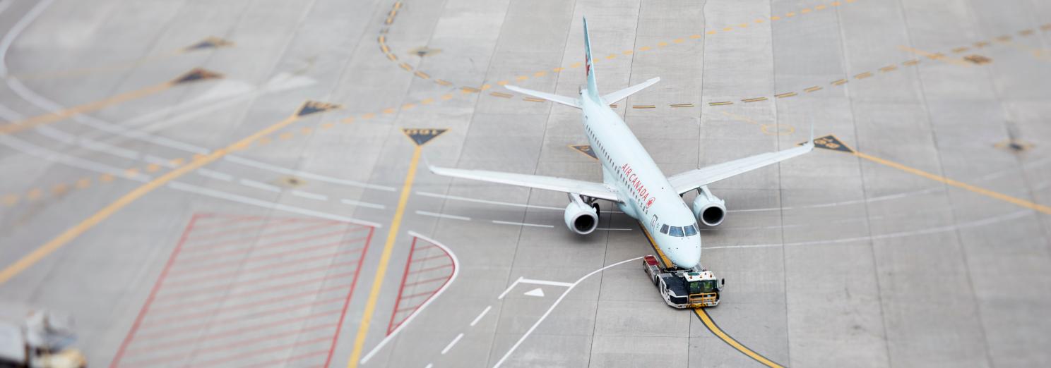 An airplane on the runway at the Toronto Pearson airport. It's being towed by a small vehicle.